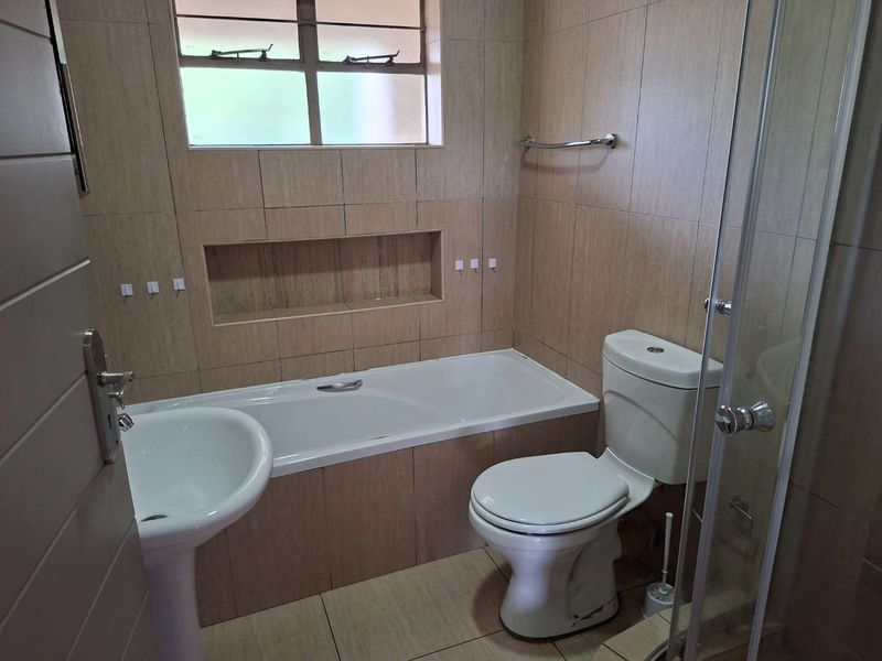 A functional bathroom featuring a pedestal basin, built-in bathtub with a recessed niche, toilet, and a glass-enclosed shower with neutral wall tiling.