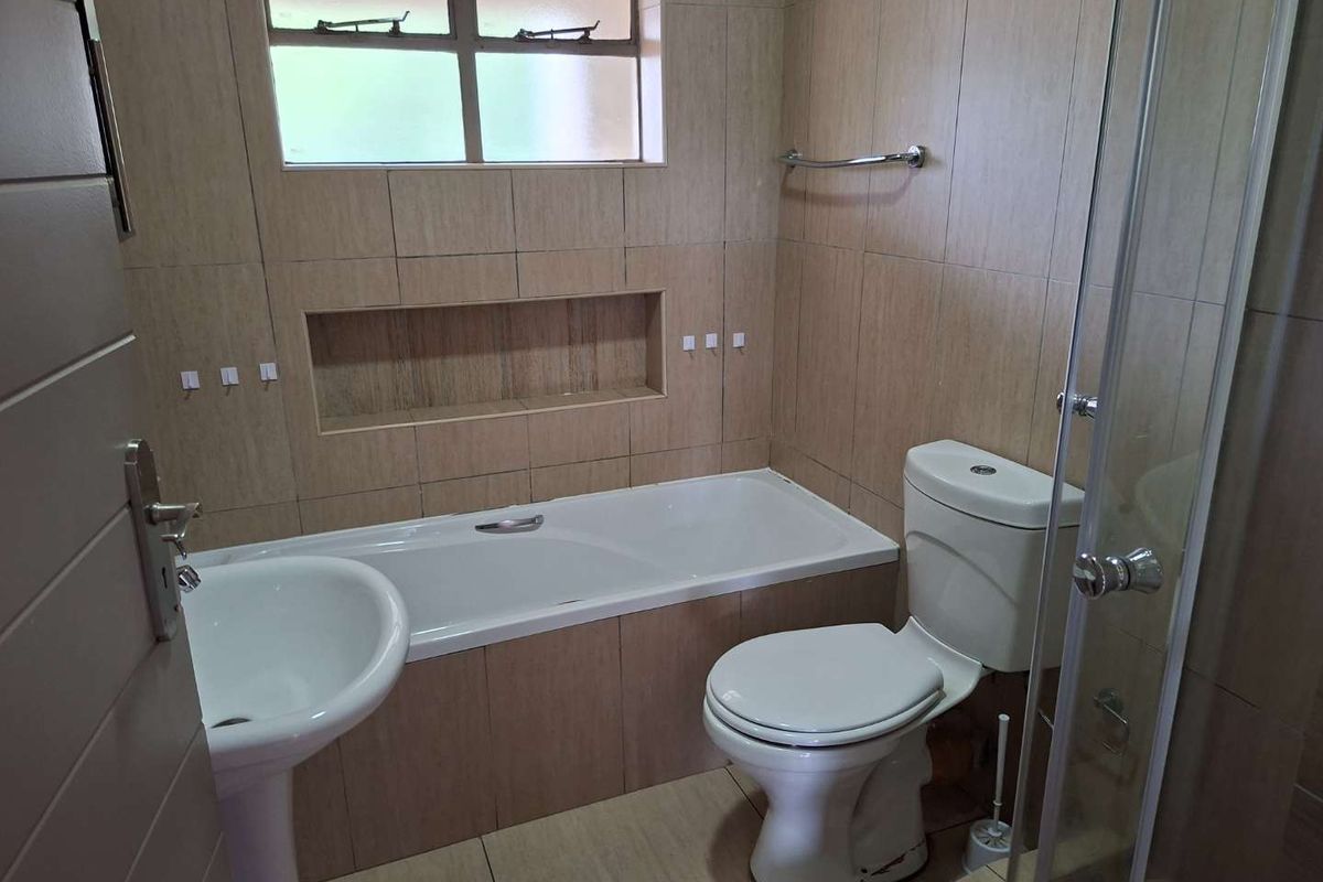 A functional bathroom featuring a pedestal basin, built-in bathtub with a recessed niche, toilet, and a glass-enclosed shower with neutral wall tiling.