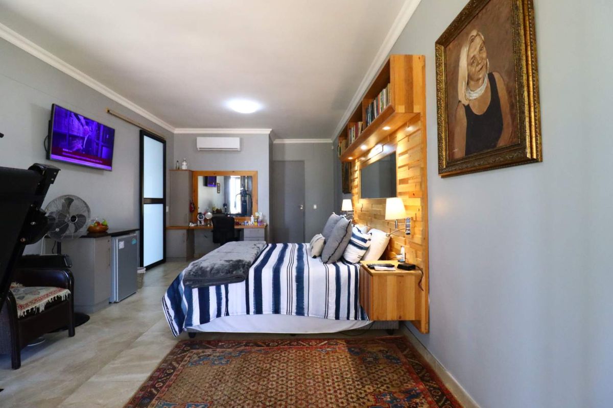 Spacious bedroom featuring a built-in timber headboard with integrated shelving and lighting, tiled flooring, and a wall-mounted air conditioning unit.