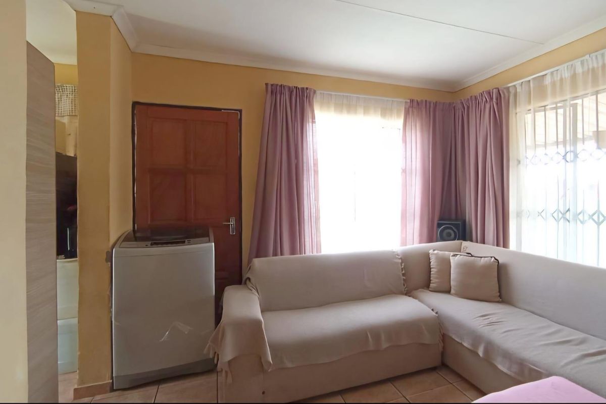 A living room area featuring tiled flooring, large windows with curtains, and a solid timber door.