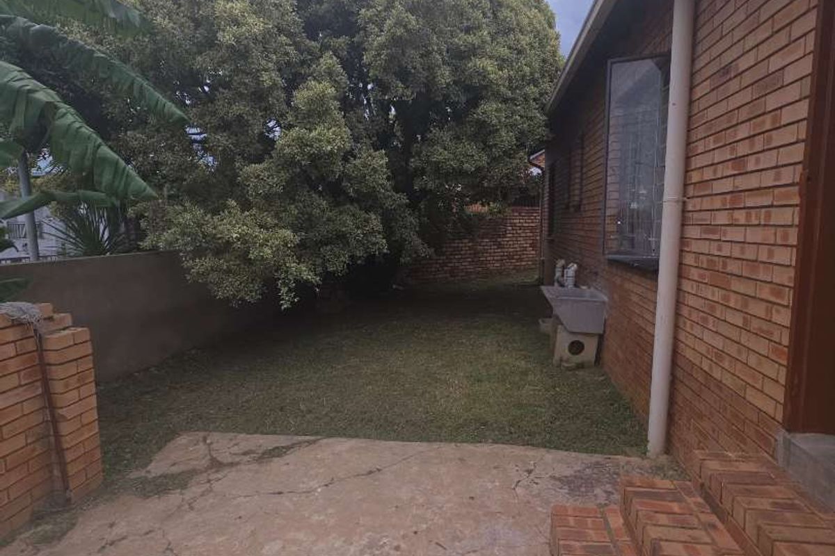 A rear garden area featuring a concrete patio, brick steps, and established trees, providing a private outdoor space adjacent to the house.