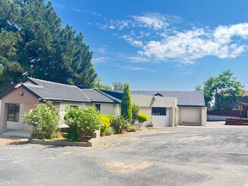 Front view of a single-story house featuring a tiled roof, attached garage, and a spacious asphalt driveway with established garden landscaping.