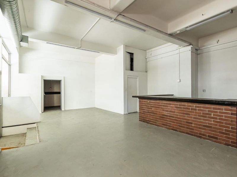 An open-plan industrial style space featuring exposed ducting, concrete flooring, and a built-in brick counter, suitable for a variety of commercial or creative uses.
