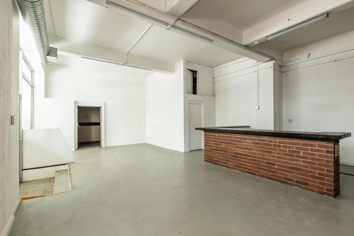An open-plan industrial style space featuring exposed ducting, concrete flooring, and a built-in brick counter, suitable for a variety of commercial or creative uses.