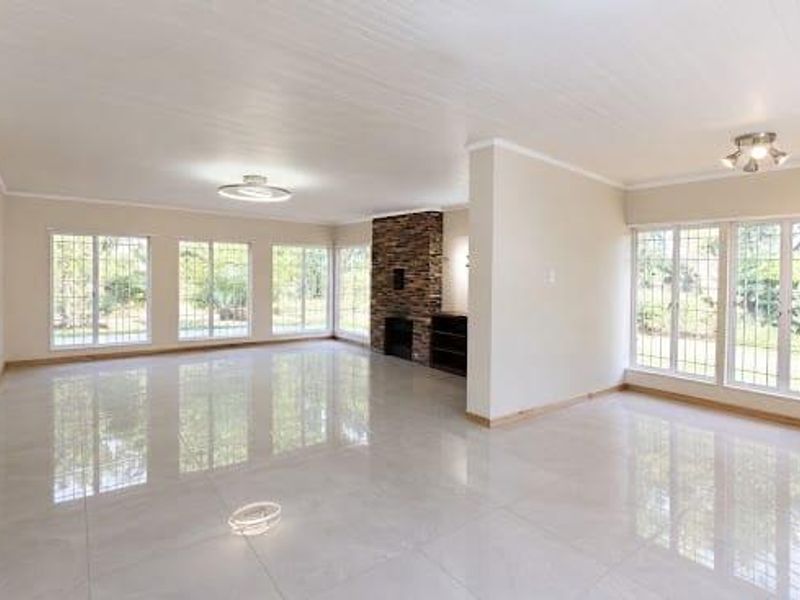 Spacious, light-filled living area featuring polished tiled floors, a striking stone-clad fireplace, and large windows with security bars.
