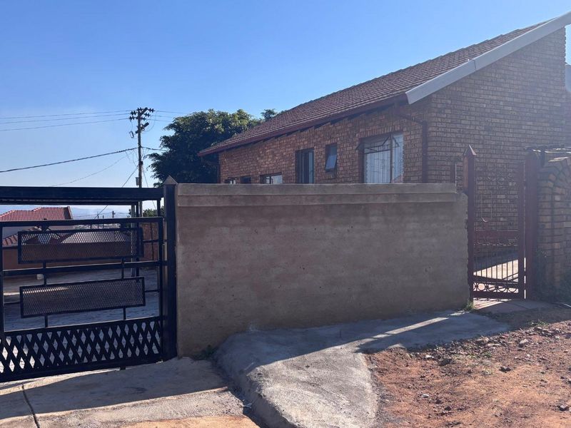 Front exterior view of a face brick house featuring a secure perimeter wall, metal driveway gate, and pedestrian access gate.