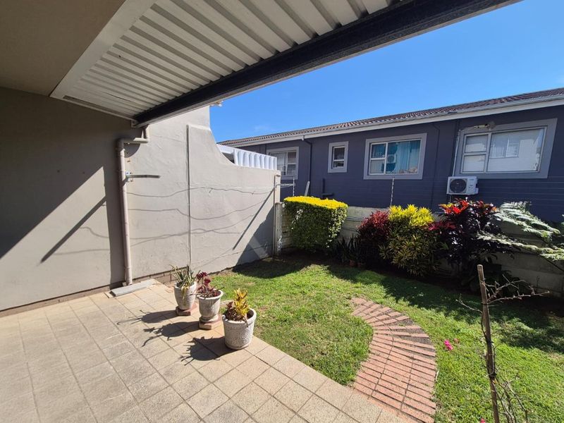 A covered patio area overlooking a private garden with a brick pathway, lawn, and boundary wall, providing a pleasant outdoor space.