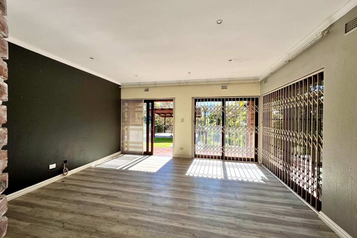 Spacious living area featuring modern laminate flooring, recessed lighting, and large sliding glass doors with security gates leading to the outdoor patio.