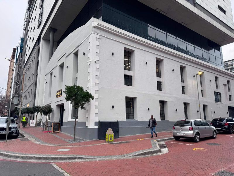 Street-level view of a modern commercial building featuring a white masonry facade with recessed windows and an integrated glass-fronted upper structure.