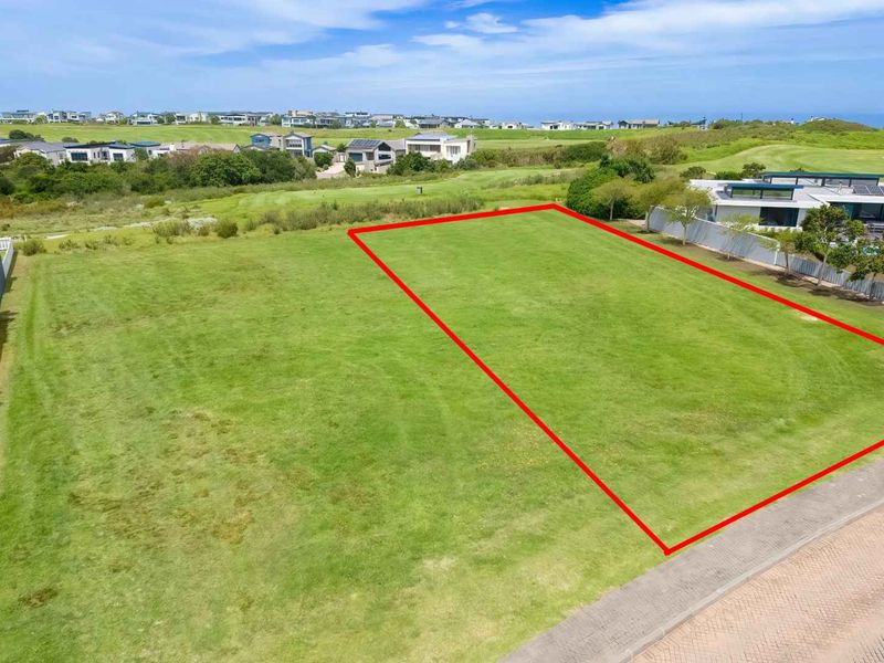 An aerial view of a vacant residential plot featuring a level grassed surface with direct access to a paved road in a coastal estate.