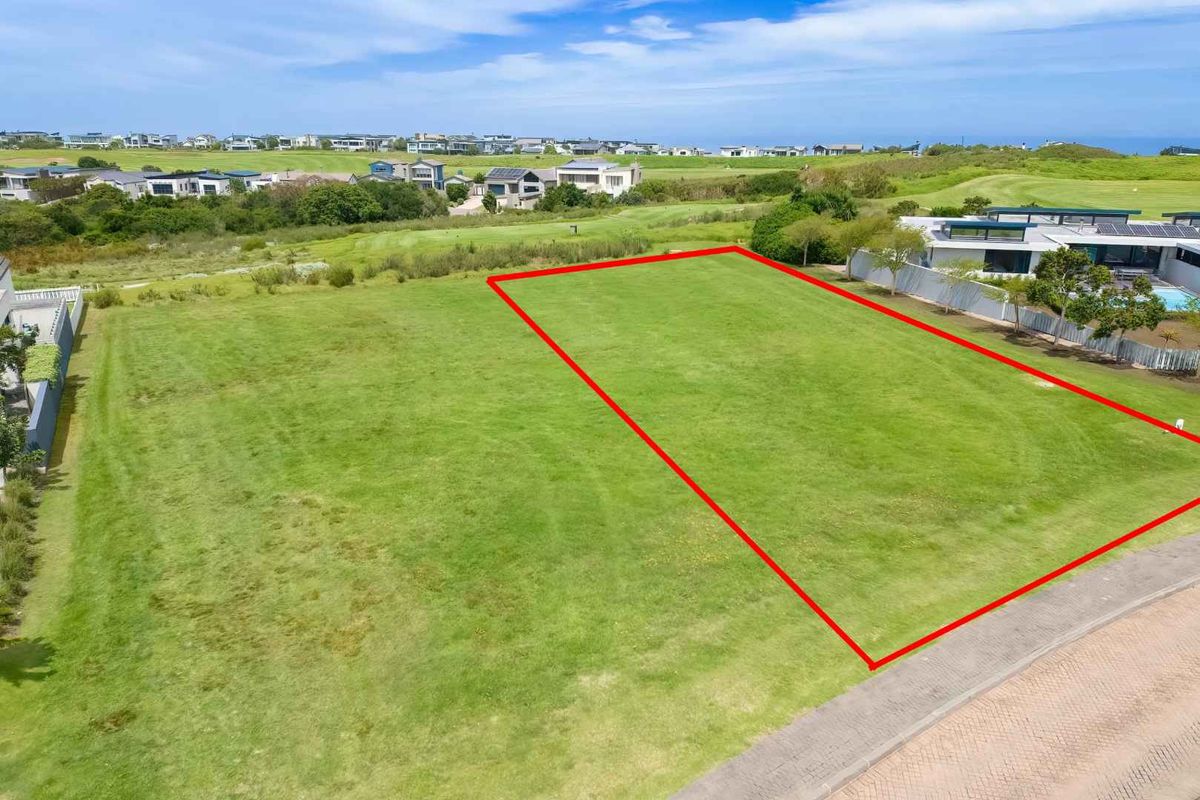 An aerial view of a vacant residential plot featuring a level grassed surface with direct access to a paved road in a coastal estate.