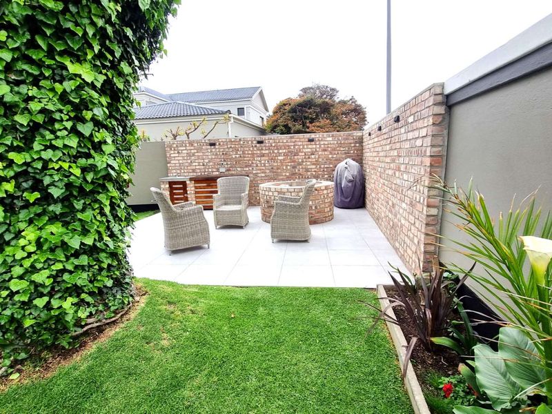 A well-maintained outdoor patio area featuring a built-in brick fire pit, a brick braai station, and paved flooring, enclosed by a private brick wall.