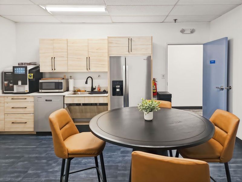 A functional office kitchenette featuring light-wood cabinetry, stainless steel appliances, a sink, and a drop ceiling, providing a convenient break area.