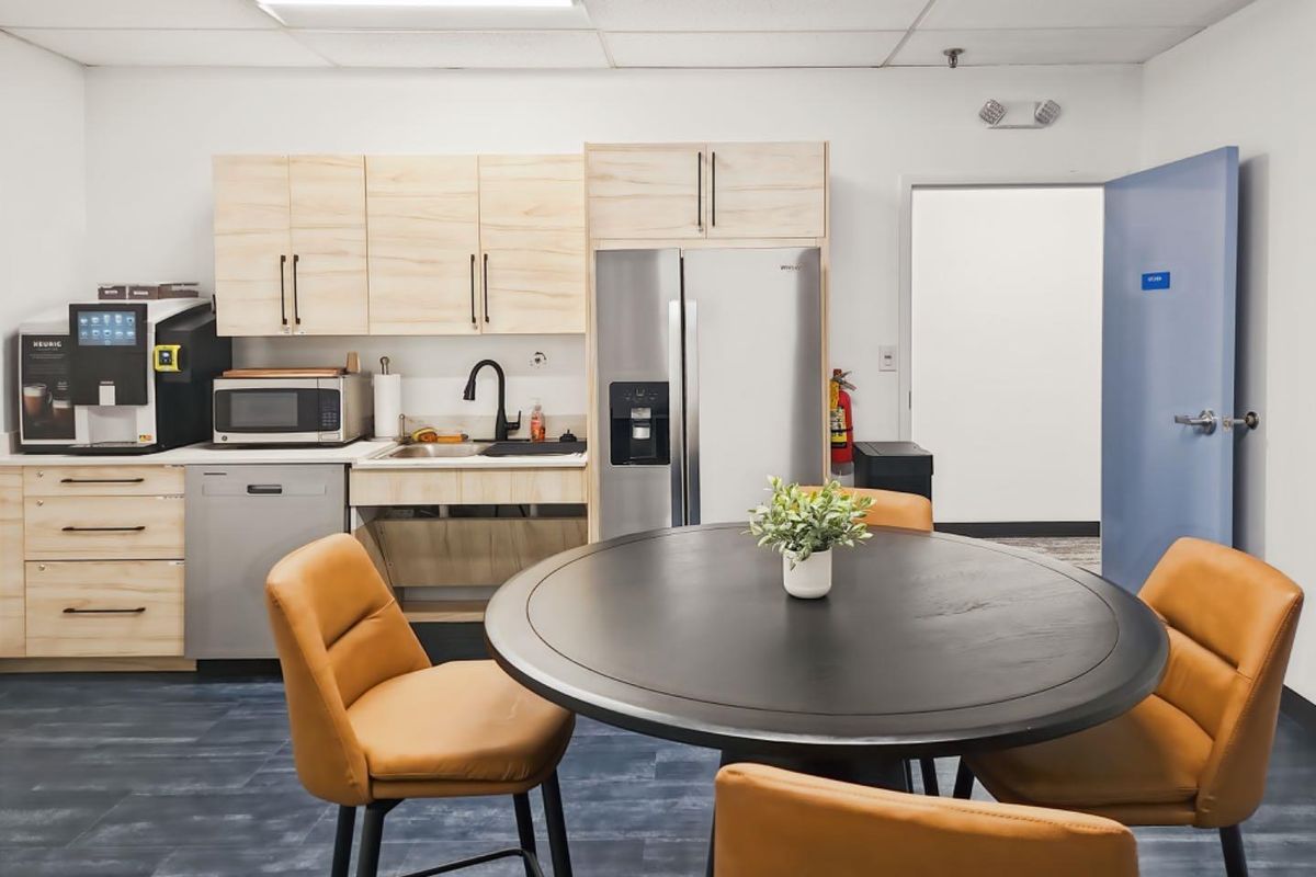 A functional office kitchenette featuring light-wood cabinetry, stainless steel appliances, a sink, and a drop ceiling, providing a convenient break area.
