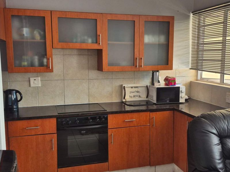 A functional kitchen featuring wood-finish cabinetry, dark countertops, a built-in electric oven and hob, and tiled backsplash with natural light from the window.