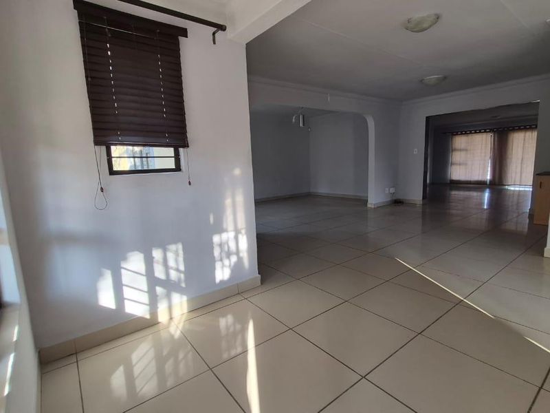 Spacious open-plan living area featuring neutral tiled flooring, clean white walls, and an arched transition between connected living spaces.