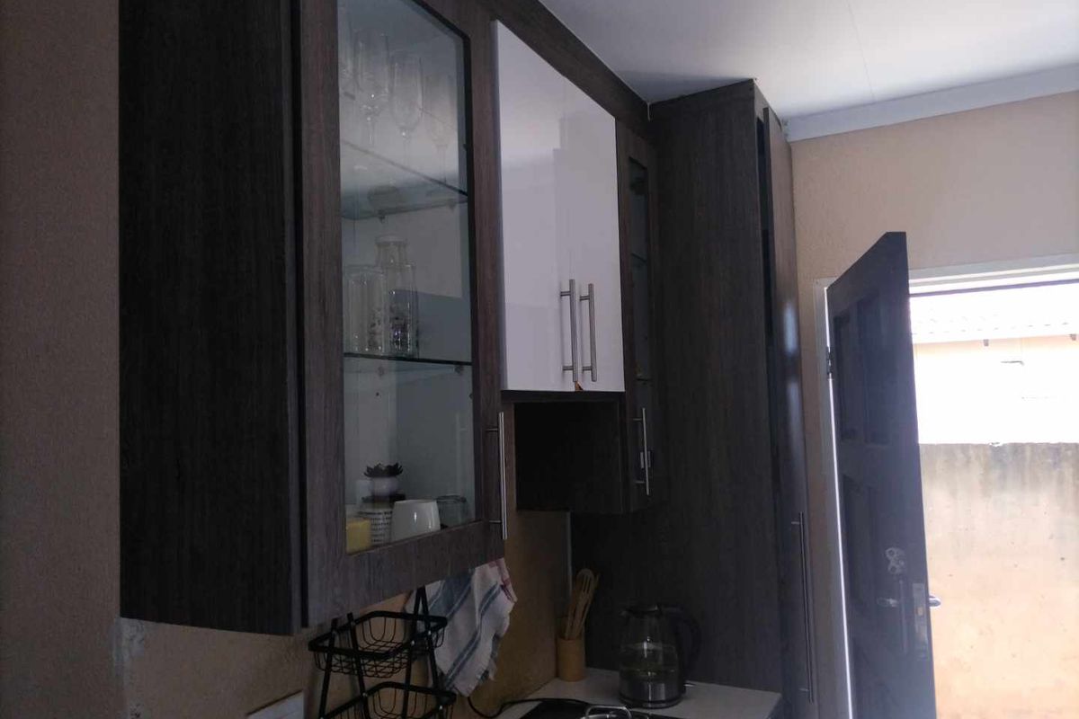 A compact kitchen area featuring dark wood-grain cabinetry, contrasting white upper cabinets, and a built-in cooktop with direct access to an exterior door.