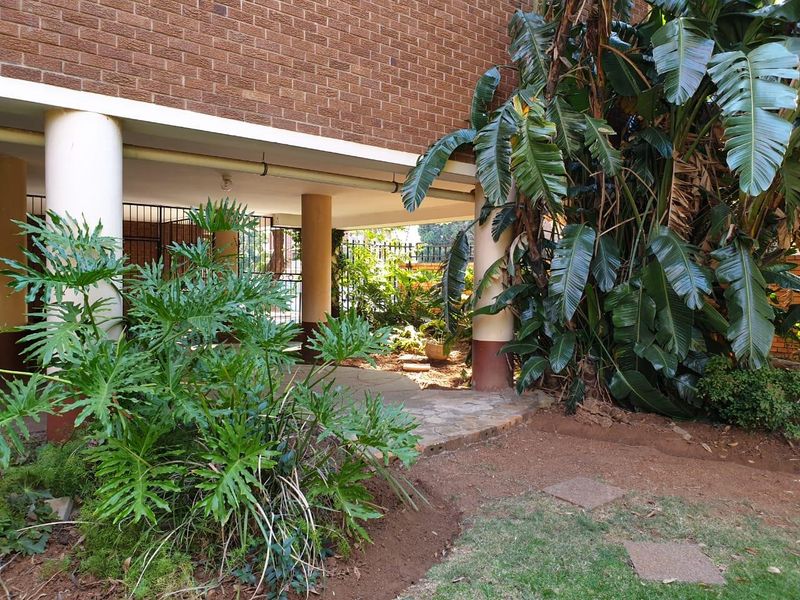 A view of the rear exterior area featuring a brick facade, concrete support columns, and a paved walkway leading to a security gate.