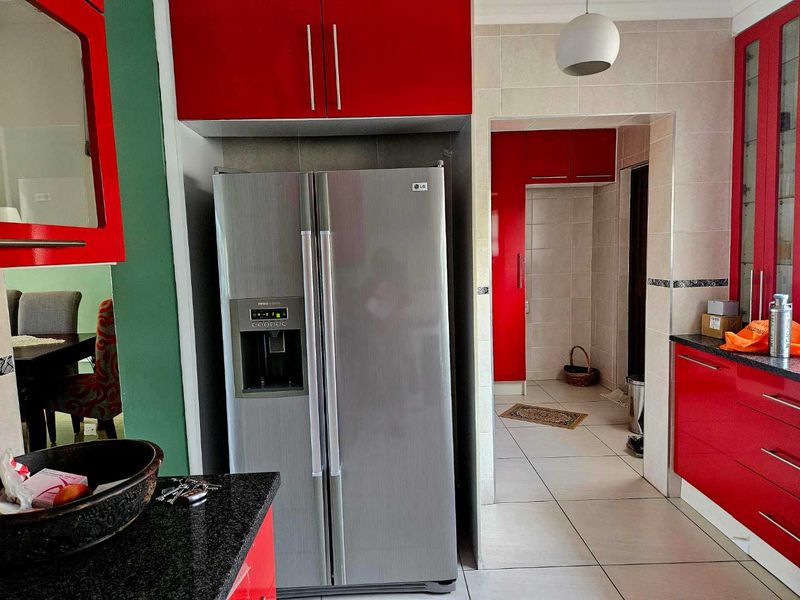 A kitchen featuring vibrant red cabinetry, granite countertops, and tiled flooring, with an adjacent pantry or scullery area.