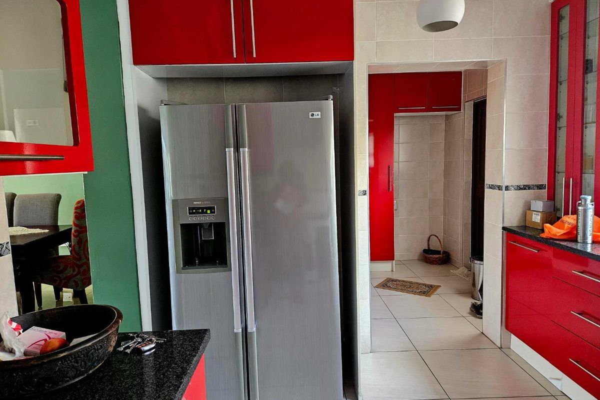 A kitchen featuring vibrant red cabinetry, granite countertops, and tiled flooring, with an adjacent pantry or scullery area.