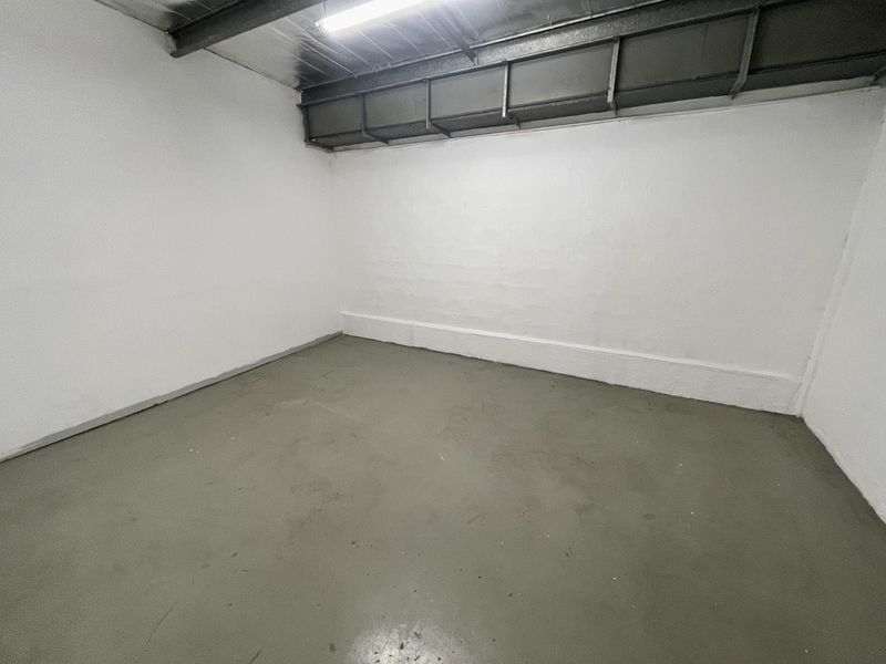 A clean, empty industrial garage space featuring painted concrete flooring, exposed steel structural beams, and functional overhead fluorescent lighting.