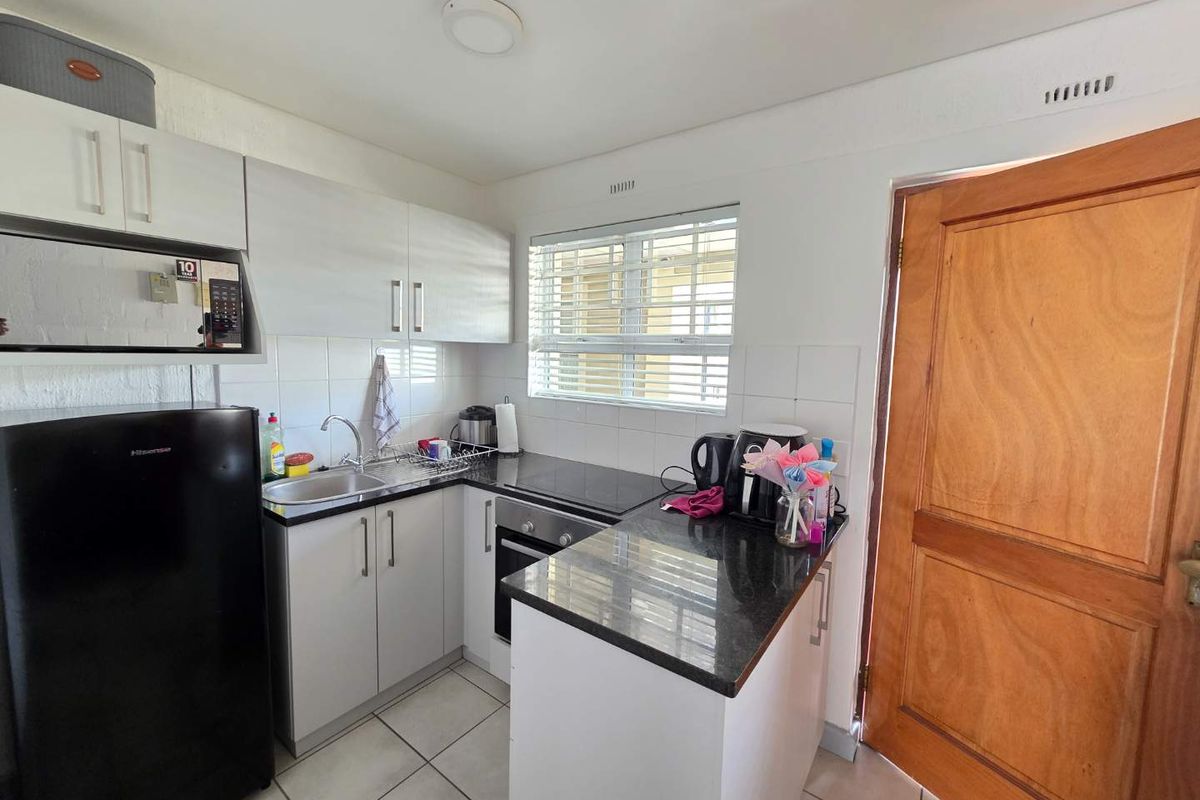 Compact kitchen featuring granite countertops, built-in oven, hob, and white cabinetry with tiled flooring and backsplash.