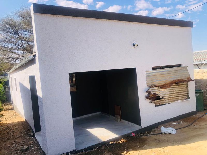 Rear view of a residential structure featuring a small tiled patio area and exterior wall lighting, currently showing signs of external damage.