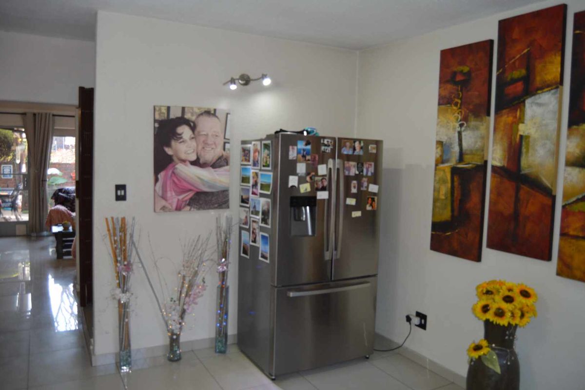 A view of a tiled interior space featuring a stainless steel refrigerator and access to an adjacent room.