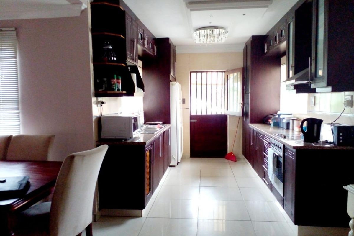 A functional kitchen featuring dark wood cabinetry, granite countertops, built-in appliances, and tiled flooring, leading to an exterior door with a security gate.