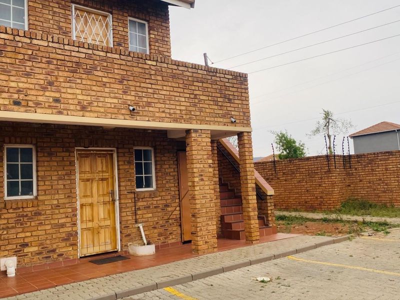 Exterior view of a face brick apartment building featuring a tiled patio, external staircase, and secure perimeter wall with electric fencing.