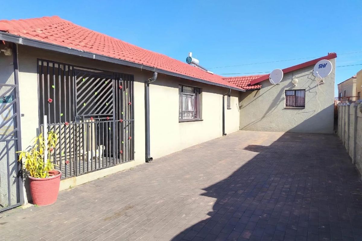 Rear exterior view of the property featuring a paved courtyard, security gates, and installed solar water heating system.