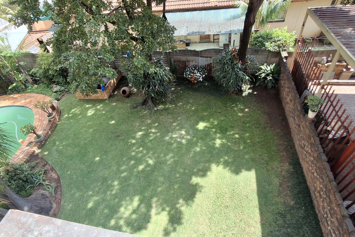 An elevated aerial view of a private backyard featuring a swimming pool, a well-maintained lawn, and a brick boundary wall.