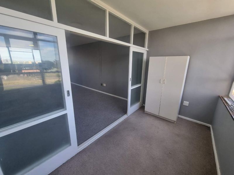 A bedroom featuring sliding glass partition doors with transom windows, carpeted flooring, and neutral grey walls, offering a flexible layout.