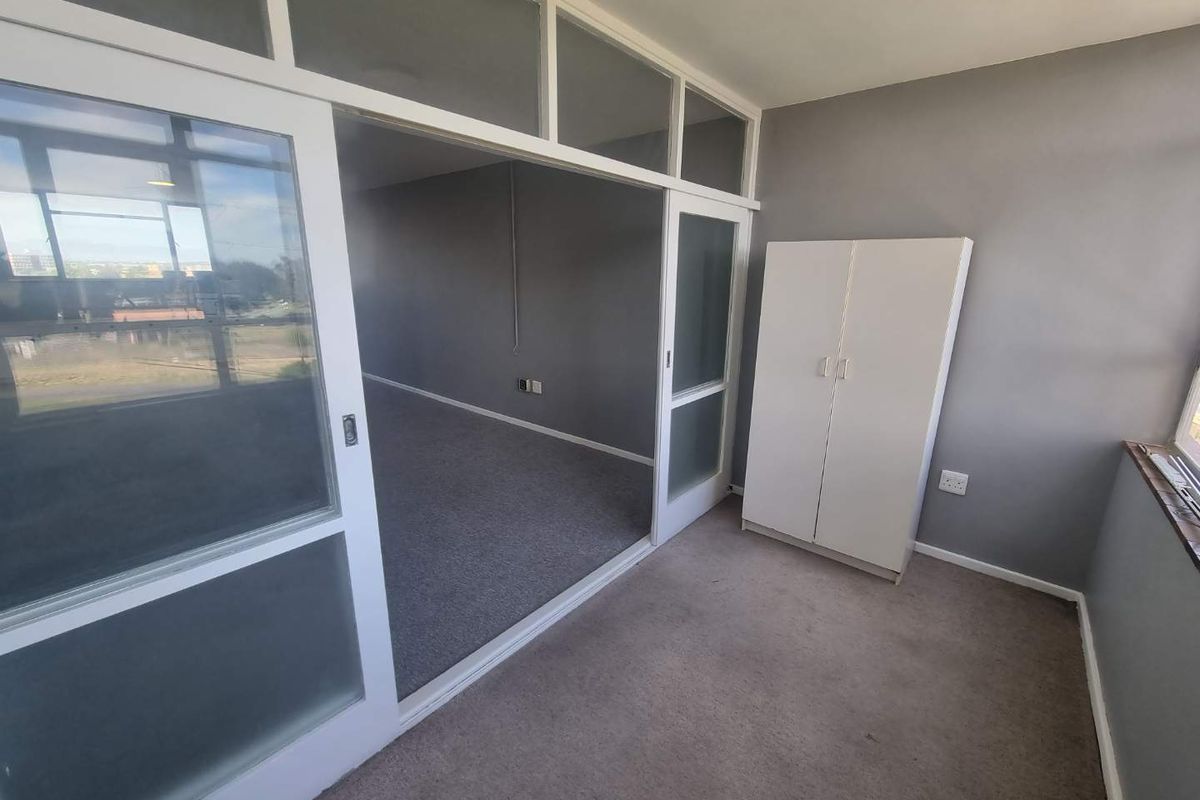 A bedroom featuring sliding glass partition doors with transom windows, carpeted flooring, and neutral grey walls, offering a flexible layout.