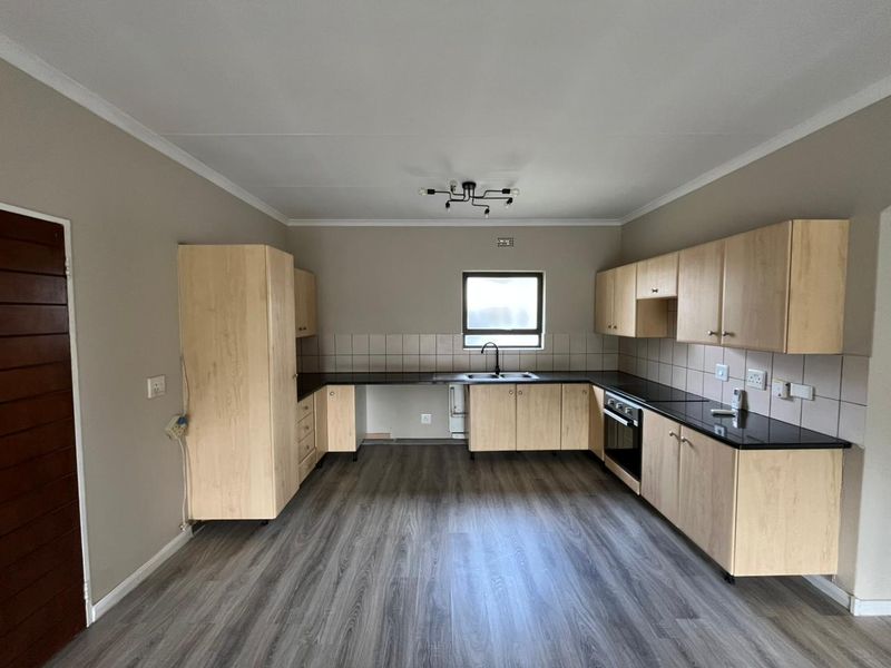 A functional kitchen featuring light wood cabinetry, dark laminate countertops, built-in oven, and durable laminate flooring in an open, vacant space.