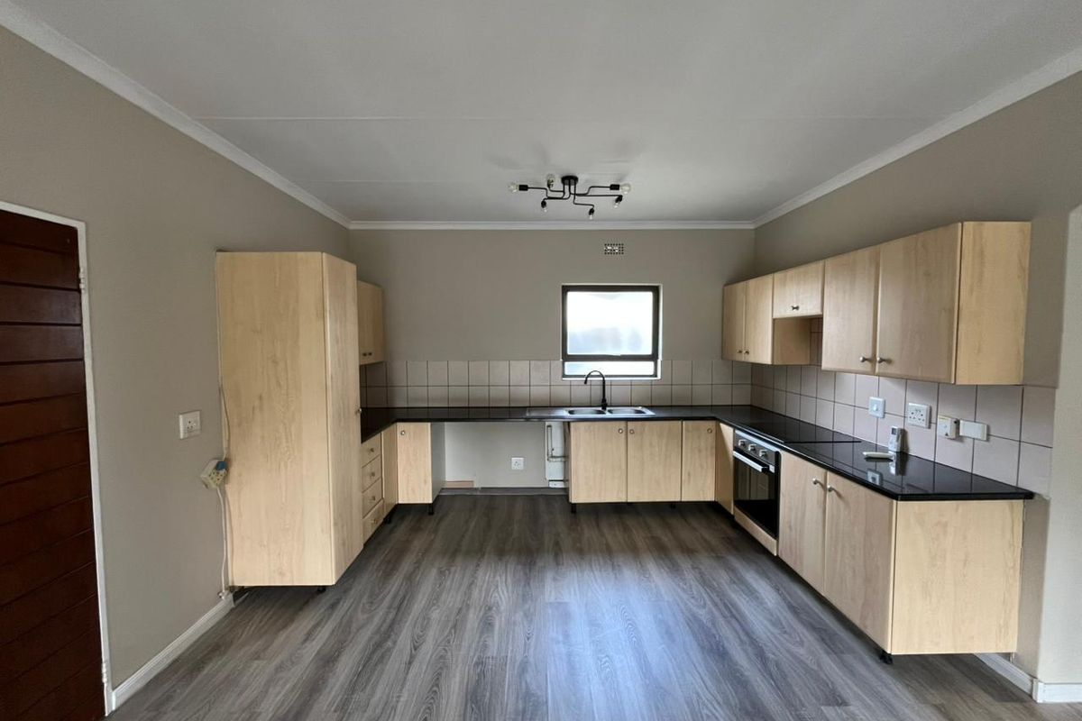 A functional kitchen featuring light wood cabinetry, dark laminate countertops, built-in oven, and durable laminate flooring in an open, vacant space.