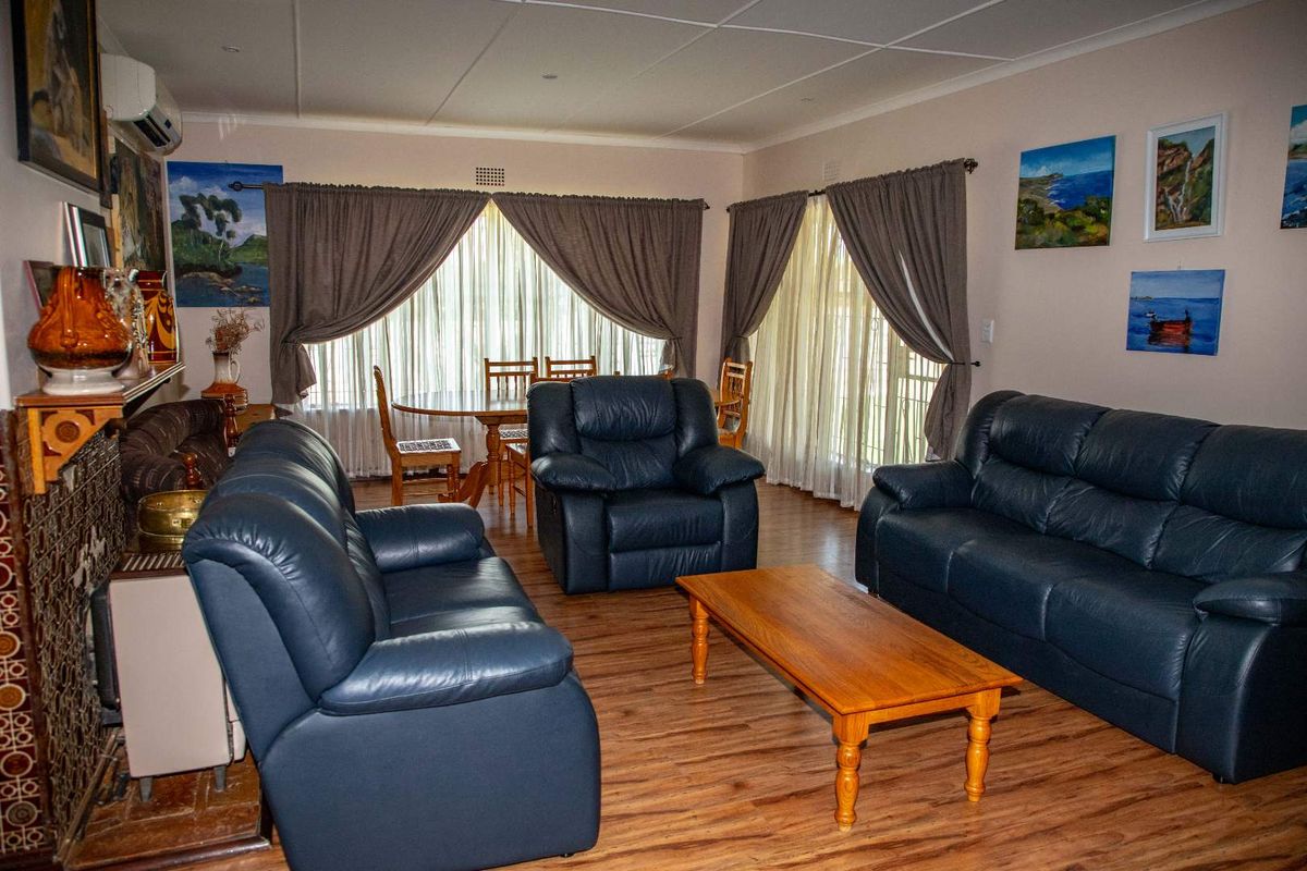 A spacious living room featuring wood-look flooring, a tiled fireplace surround, and large windows with curtains, providing a comfortable and functional living space.
