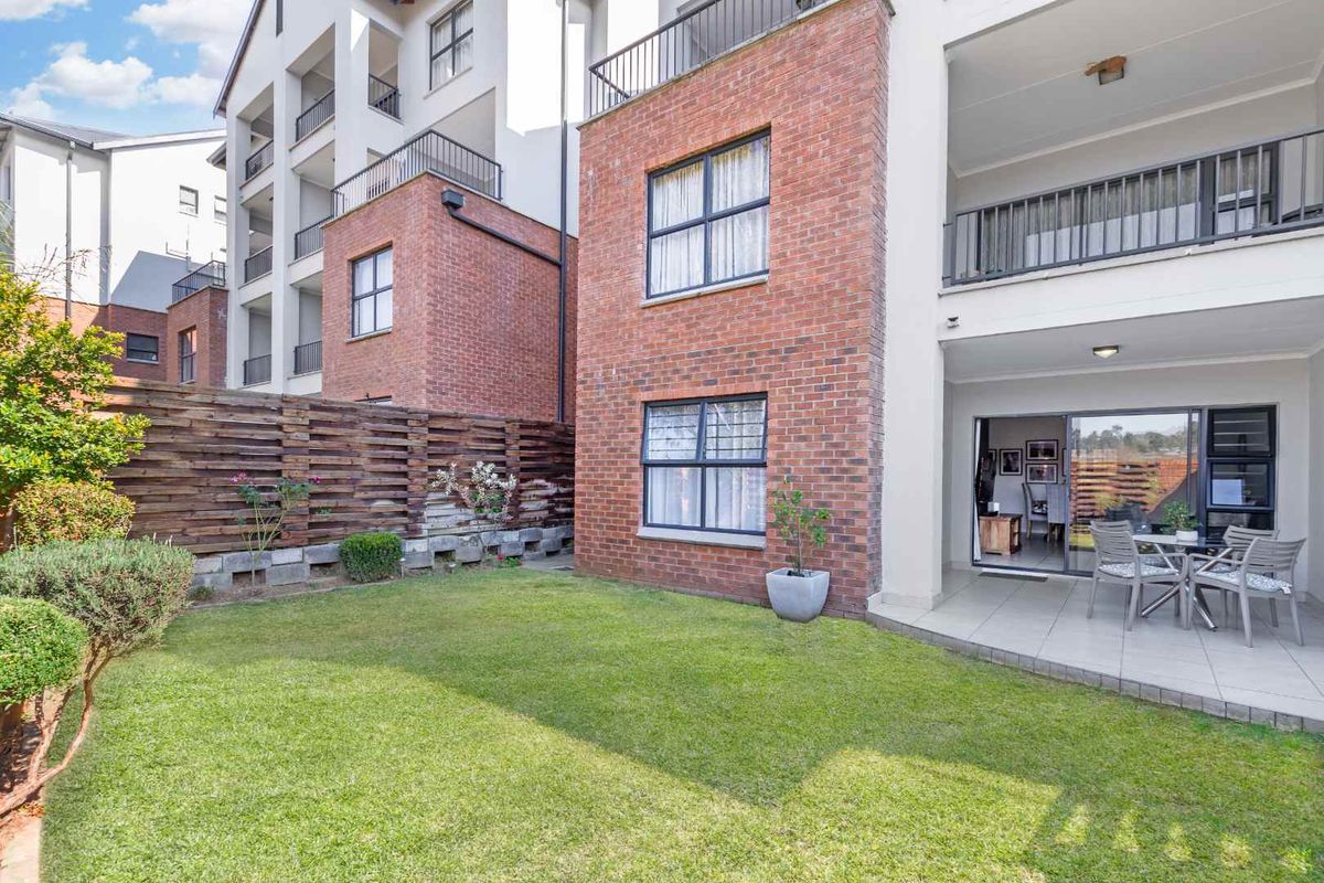 Rear view of the apartment featuring a private garden, tiled patio area, and brick facade with sliding door access to the living space.
