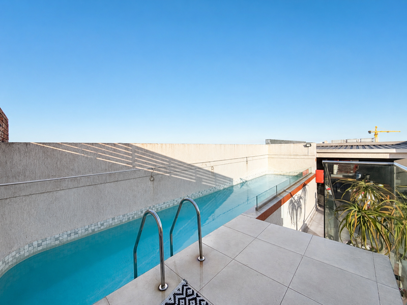 A rooftop lap pool featuring a glass balustrade, tiled decking, and a stainless steel ladder, offering a clean and modern outdoor space.