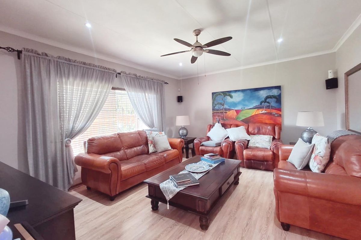 A comfortable living room featuring light-toned laminate flooring, a central ceiling fan, and recessed downlighting, creating a warm and inviting atmosphere.