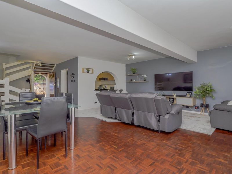 Spacious open-plan living and dining area featuring classic parquet flooring, a central structural beam, and an arched entryway leading to the kitchen.
