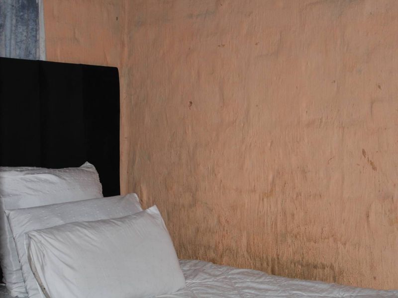 A bedroom interior featuring a textured wall with visible surface staining and deterioration, requiring maintenance or refinishing.