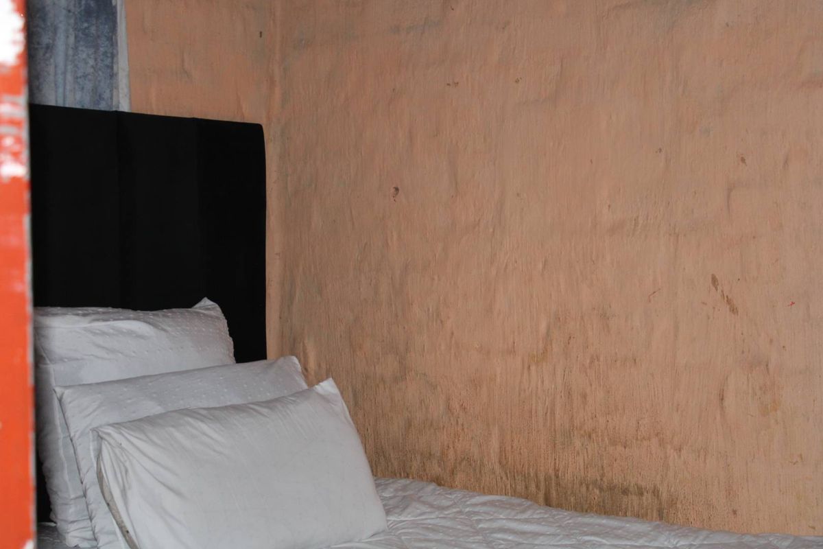 A bedroom interior featuring a textured wall with visible surface staining and deterioration, requiring maintenance or refinishing.