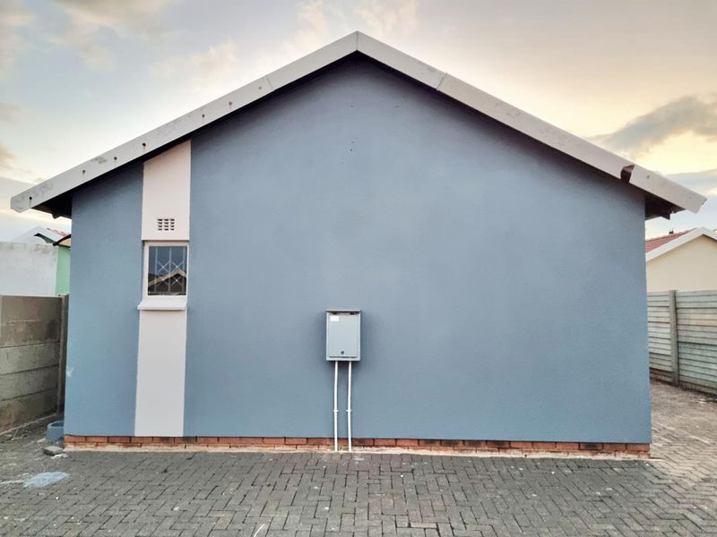 A clean rear exterior elevation featuring a gable roof, paved ground area, and an external electrical distribution board.