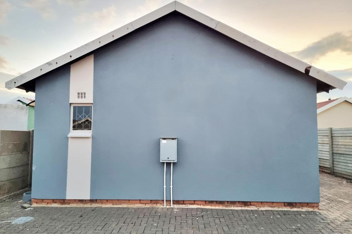 A clean rear exterior elevation featuring a gable roof, paved ground area, and an external electrical distribution board.
