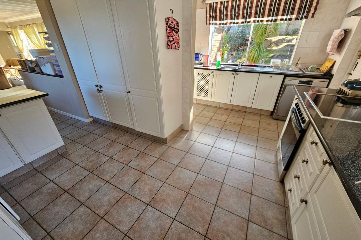 A functional kitchen featuring white cabinetry, granite countertops, tiled flooring, and integrated appliances, with a window overlooking the rear garden area.