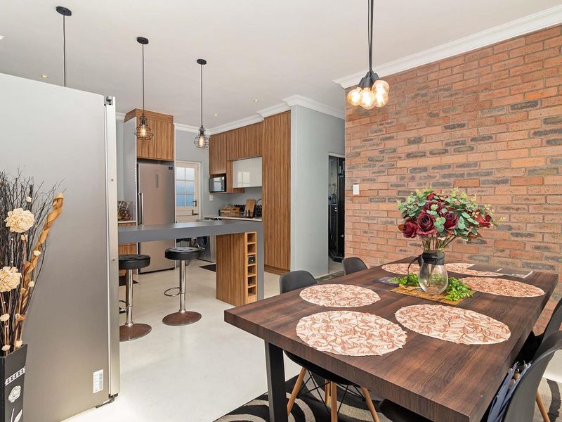 Open plan kitchen and dining area featuring a striking exposed brick feature wall, modern wood-grain cabinetry, and a functional breakfast bar.