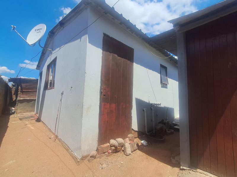 Rear exterior view of the property showing basic wall construction, a satellite dish, and exposed plumbing fixtures.