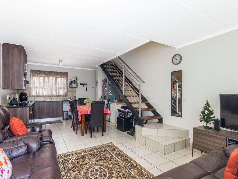 Open-plan living and dining area featuring tiled flooring, a functional kitchen, and a staircase with a modern metal railing.