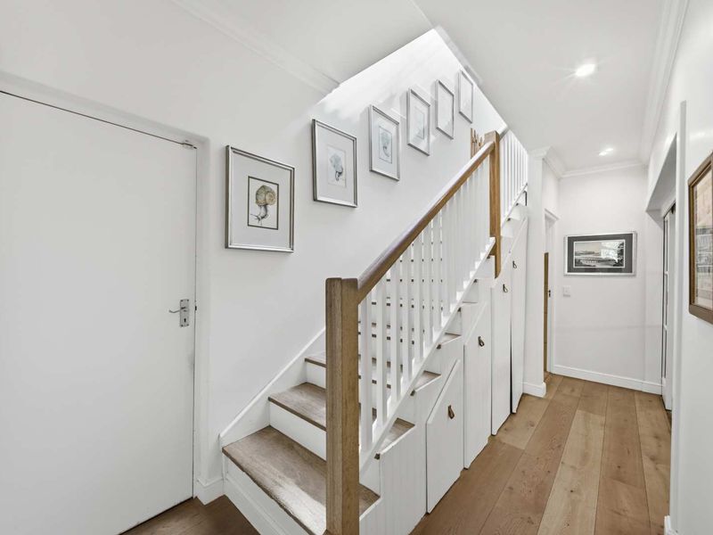 A bright, well-maintained hallway featuring a timber staircase with integrated under-stair storage cabinetry and high-quality timber flooring.